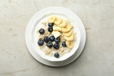 Photo of Tasty oatmeal with banana, blueberries, butter and milk served in bowl on light grey table, top view. Space for text