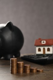 House model, piggy bank, calculator and stacked coins on wooden table, selective focus