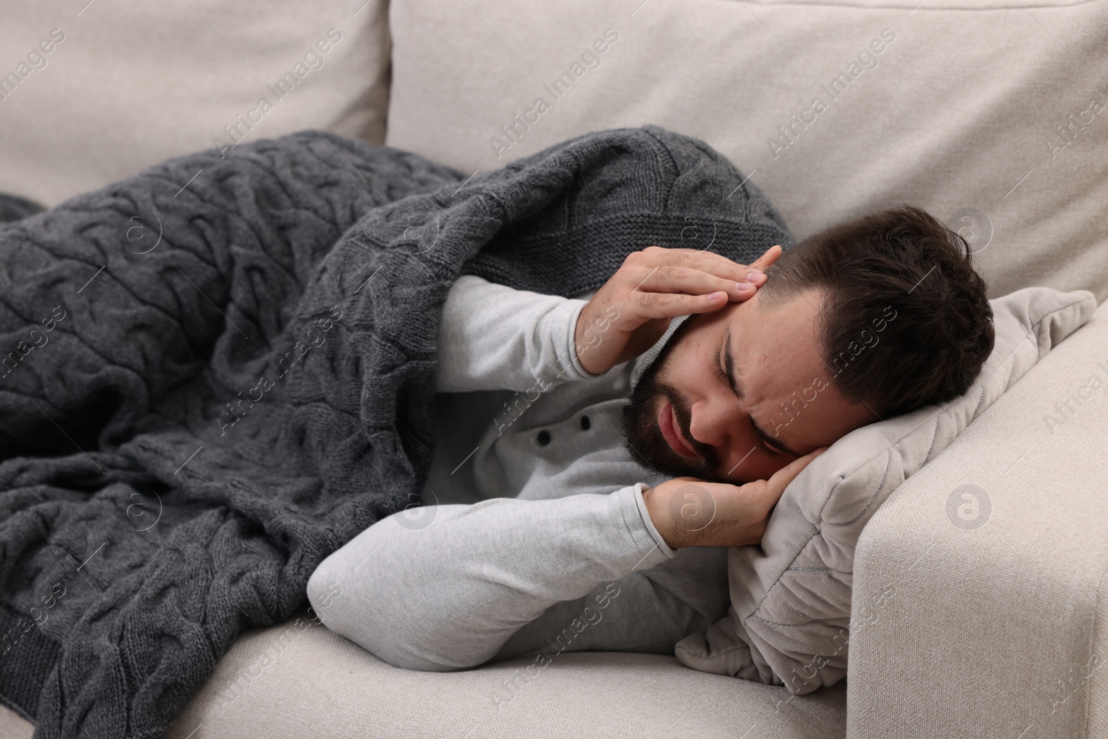 Photo of Man suffering from headache on sofa under blanket