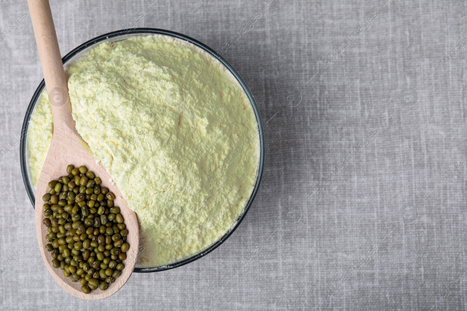 Photo of Bowl of flour, spoon and mung beans on light grey cloth, top view. Space for text