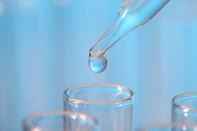 Photo of Laboratory analysis. Dripping liquid from pipette into glass test tube on light blue background, closeup