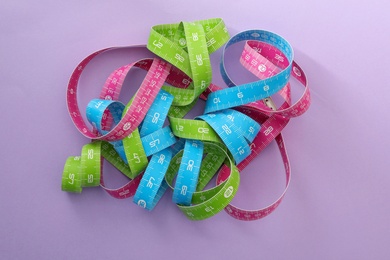 Photo of Kit of different measuring tapes on purple background, flat lay