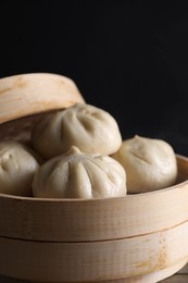 Photo of Delicious bao buns (baozi) in bamboo steamer on table against black background, closeup