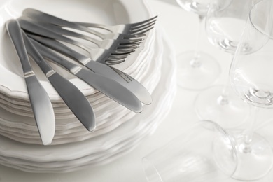 Photo of Stacked plates with cutlery and glasses on white table, closeup