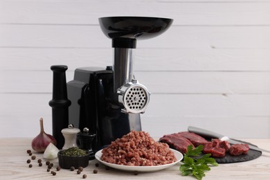 Photo of Electric meat grinder with beef, spices and parsley on white wooden table