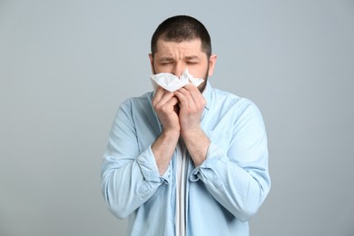 Man with tissue suffering from runny nose on light grey background