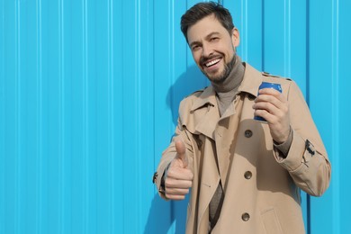 Photo of Handsome man holding tin can with beverage and showing thumbs up near light blue wall. Space for text