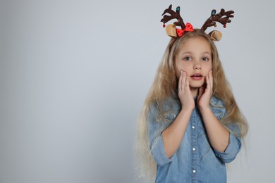 Photo of Excited girl wearing decorative Christmas headband on light grey background, space for text