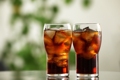 Photo of Glasses of cola with ice on table against blurred background