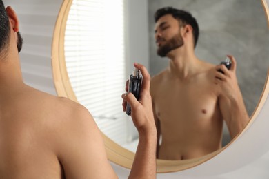 Photo of Man spraying luxury perfume near mirror indoors