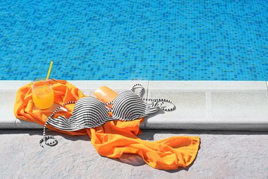 Photo of Glass of refreshing drink and different beach accessories near outdoor swimming pool on sunny day, space for text