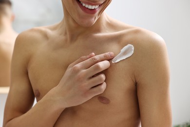 Photo of Man applying moisturizing cream onto his shoulder indoors, closeup