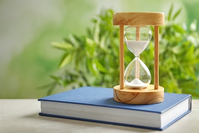 Photo of Hourglass and book on table against blurred background. Time management