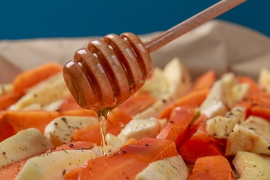 Pouring honey onto slices of parsnip and carrot against blue background, closeup