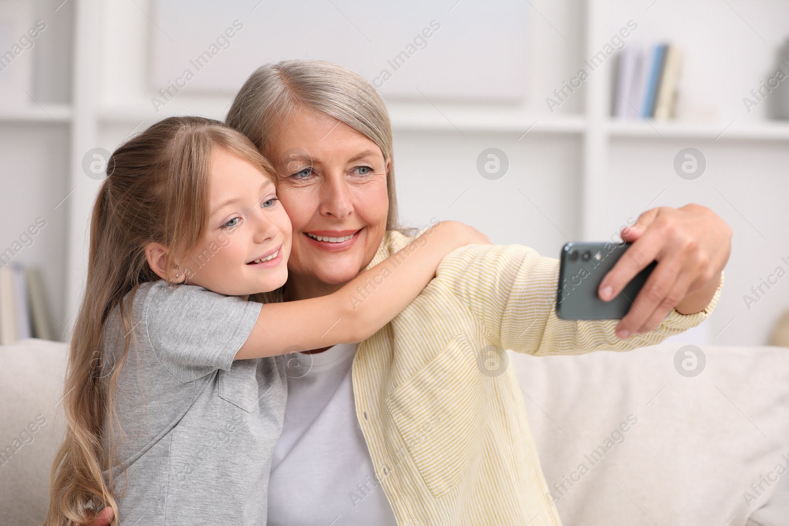 Photo of Happy grandmother taking selfie with her granddaughter at home