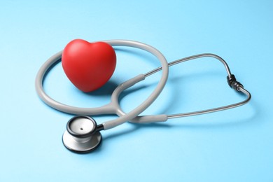 Photo of Stethoscope and red decorative heart on light blue background. Cardiology concept