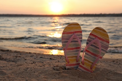 Photo of Stylish flip flops on sand near sea, space for text. Beach accessories