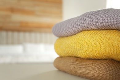 Photo of Stack of knitted sweaters on white table indoors, closeup. Space for text