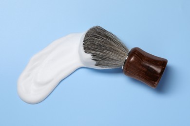 Photo of Brush with shaving foam on light blue background, top view