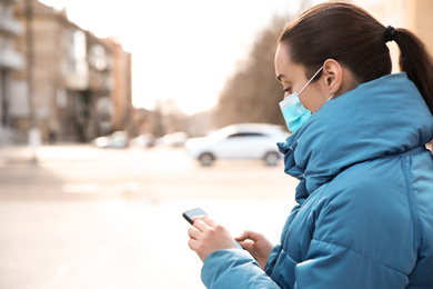 Photo of Woman with disposable mask and smartphone outdoors. Dangerous virus