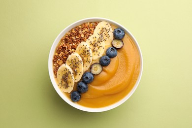 Photo of Delicious smoothie bowl with fresh blueberries, banana and granola on pale olive background, top view