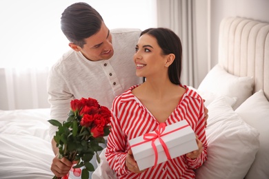 Photo of Man presenting gift and bouquet to his beloved woman at home. Valentine's day celebration