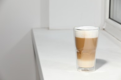 Photo of Glass with latte on white window sill. Space for text