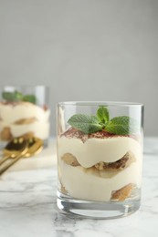 Photo of Delicious tiramisu in glass and mint leaves on white marble table