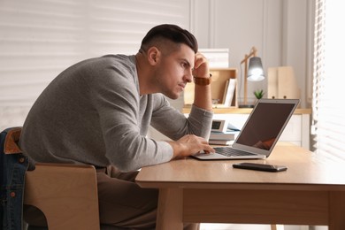 Photo of Man with poor posture using laptop at table indoors