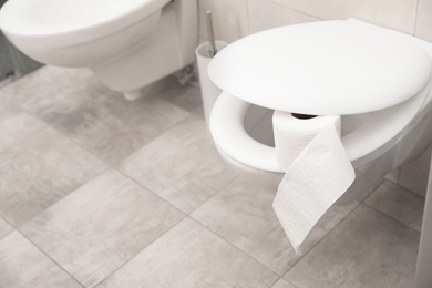 Photo of Toilet bowl with paper roll in bathroom. Space for text