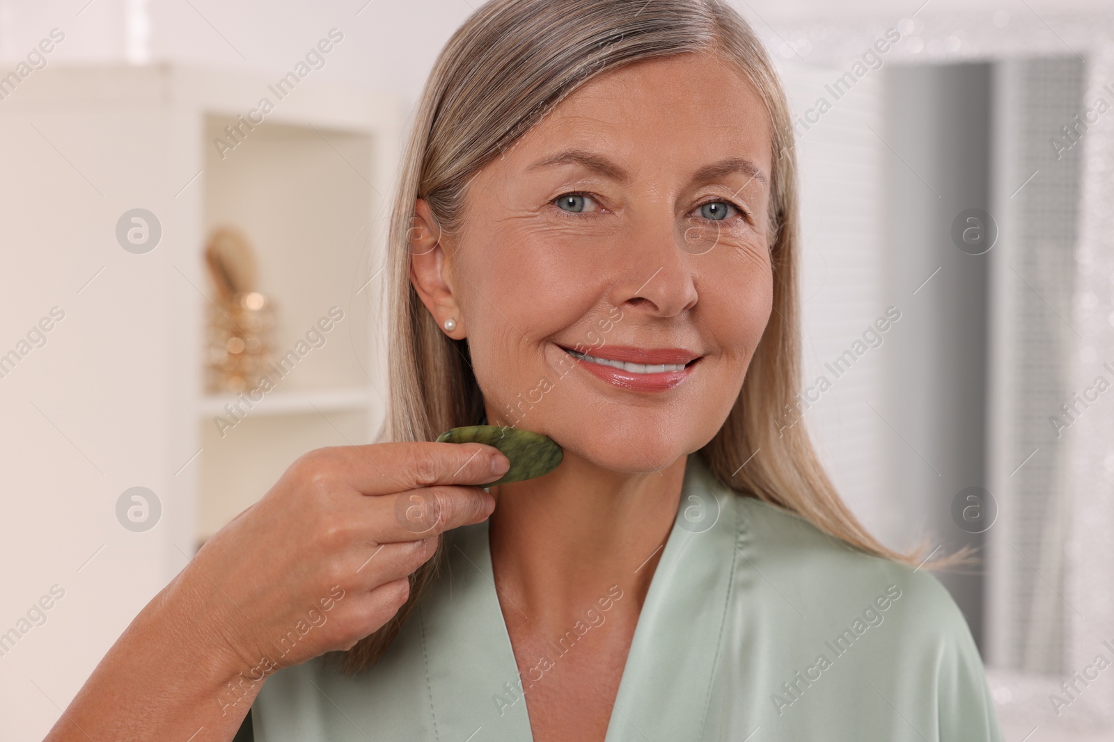 Photo of Woman massaging her face with jade gua sha tool in bathroom