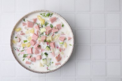 Photo of Delicious cold summer soup (okroshka) with boiled sausage in bowl on white tiled table, top view. Space for text