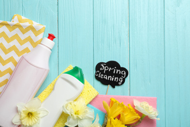 Photo of Composition with Spring Cleaning sign, flowers and detergents on light blue wooden table, flat lay. Space for text