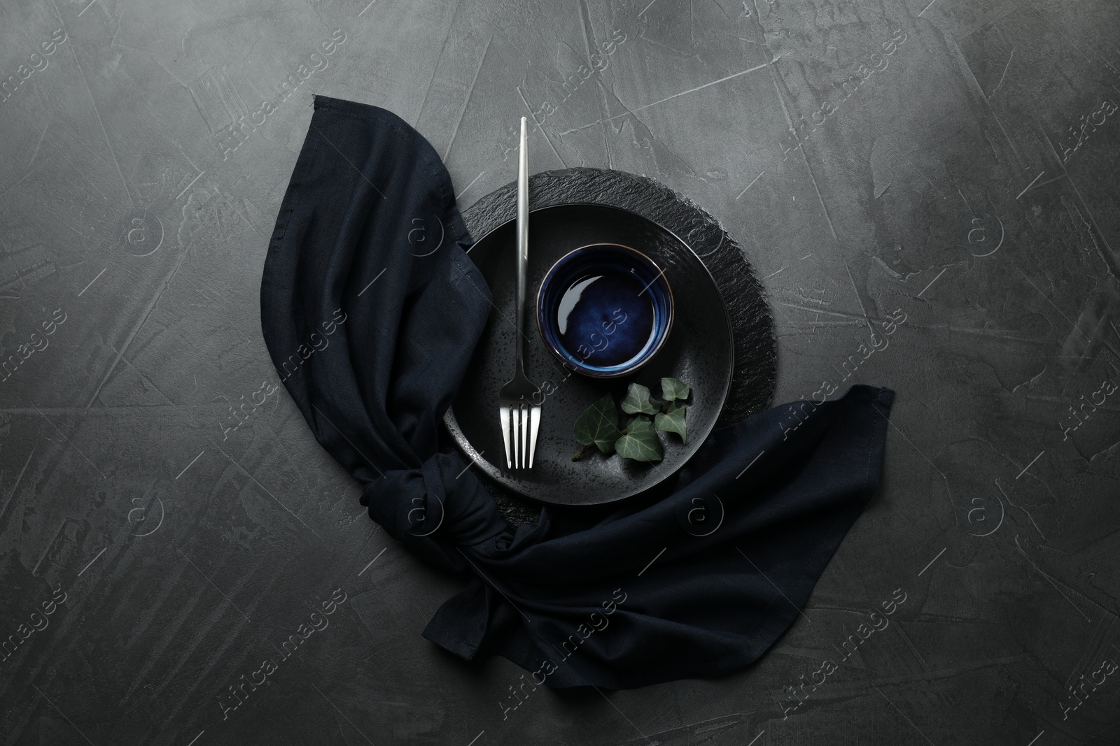 Photo of Stylish table setting. Dishes, fork, napkin and green leaves on grey surface, top view