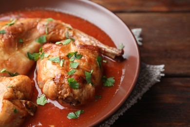 Photo of Tasty cooked rabbit meat with sauce and parsley on wooden table, closeup