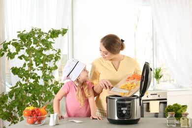 Photo of Mother and daughter preparing food with modern multi cooker in kitchen