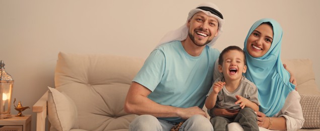 Image of Happy Muslim family on sofa in living room, space for text. Banner design 