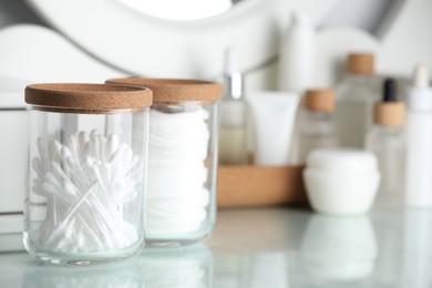 Photo of Glass jars with cotton pads and swabs on dressing table. Space for text