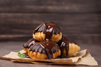 Delicious profiteroles with chocolate spread and mint on table, closeup