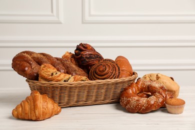 Photo of Wicker basket with different tasty freshly baked pastries on white wooden table