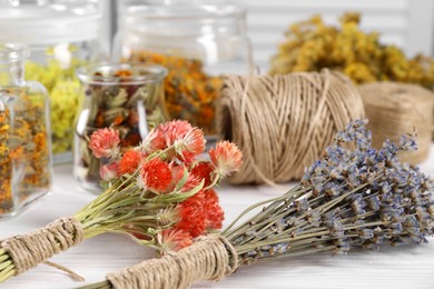 Photo of Bunches of dry flowers, different medicinal herbs and spools on white wooden table, closeup
