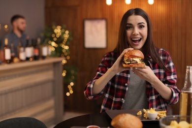 Photo of Young woman eating tasty burger in cafe