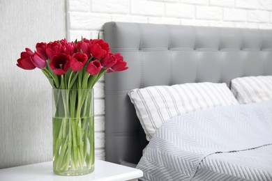 Bouquet of beautiful tulips in glass vase on white nightstand near bed
