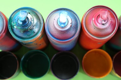 Photo of Many spray paint cans with caps on green background, above view
