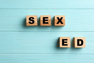 Photo of Wooden blocks with phrase "SEX ED" on light blue background, flat lay