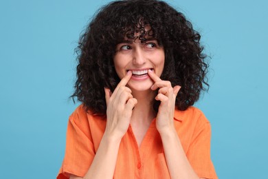 Photo of Young woman applying whitening strip on her teeth against light blue background