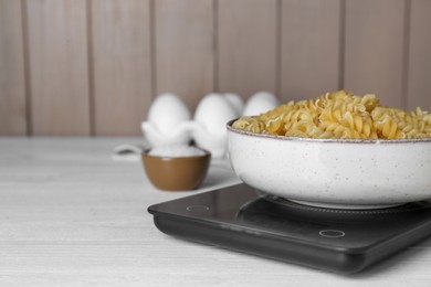 Photo of Electronic scales with uncooked pasta on white wooden table, space for text