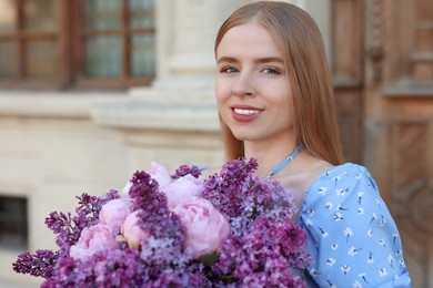 Beautiful woman with bouquet of spring flowers near building outdoors, space for text