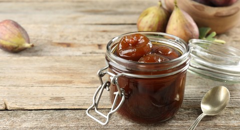 Photo of Jar of tasty sweet fig jam on wooden table. Space for text