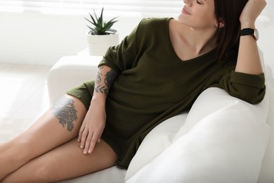 Photo of Beautiful woman with tattoos on body resting in living room, closeup